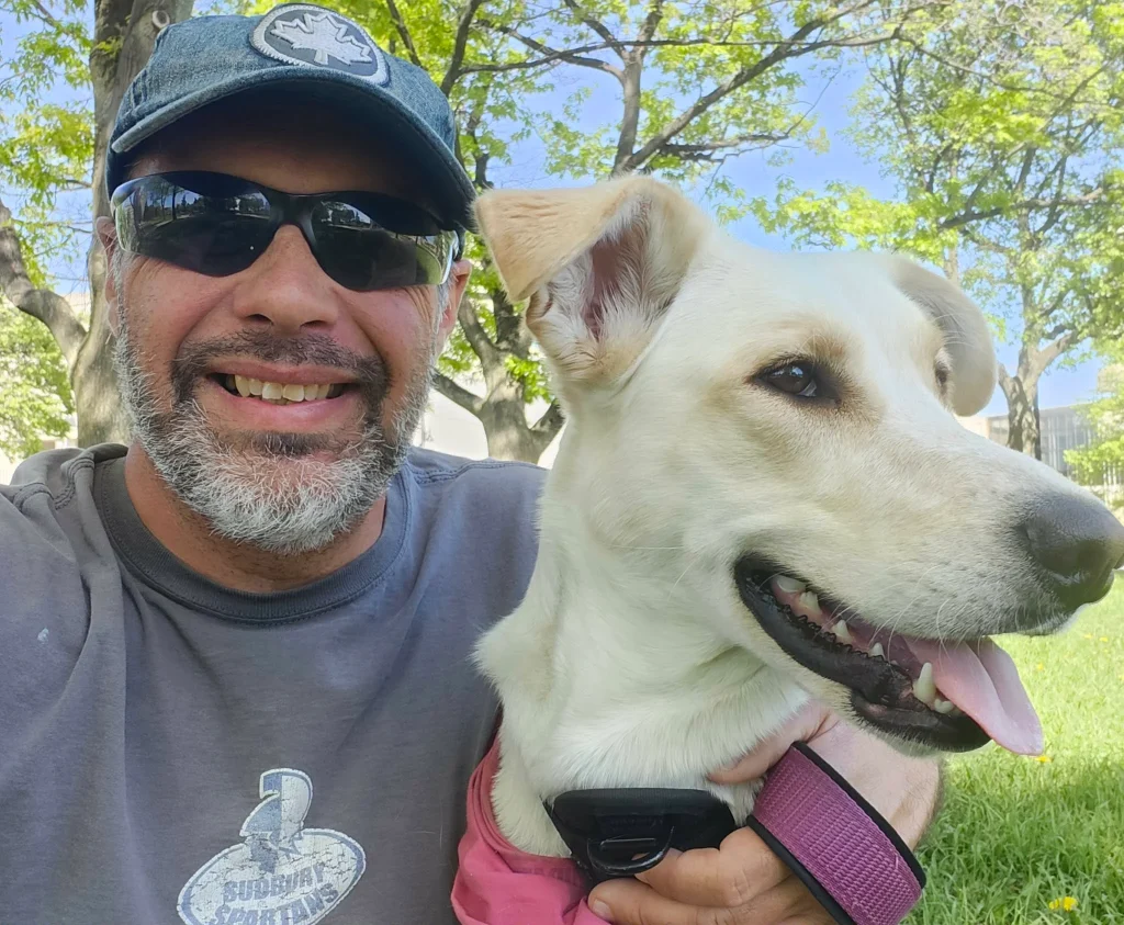 Derek Young Ward 10 Candidate poses with his dog in Bell Park, wearing sunglasses and a hat on a sunny day outside.